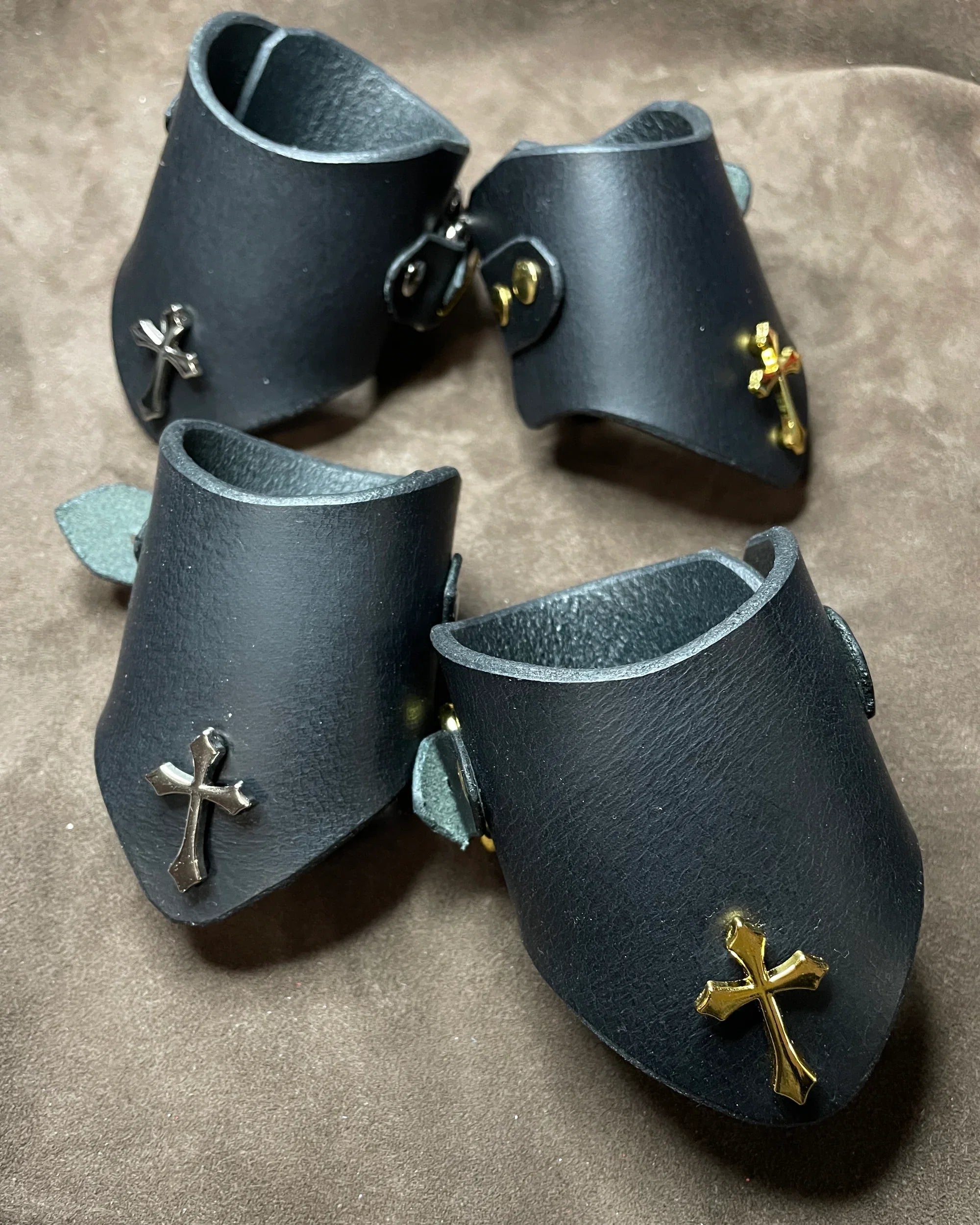 Black leather cuffs with cross embellishments on a brown surface