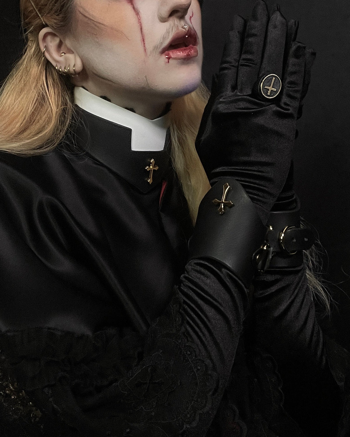 Person in black clothing with gloves, in prayer on a dark background