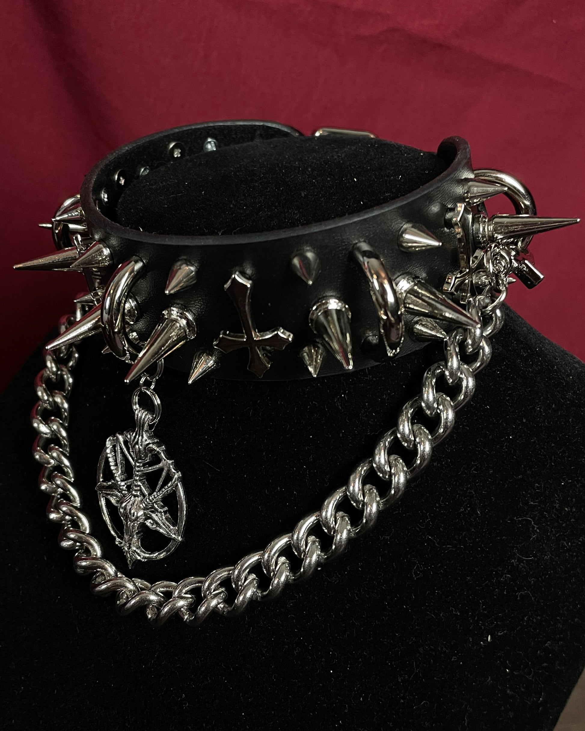 Black leather choker with spikes and chain on a black stand against a red background