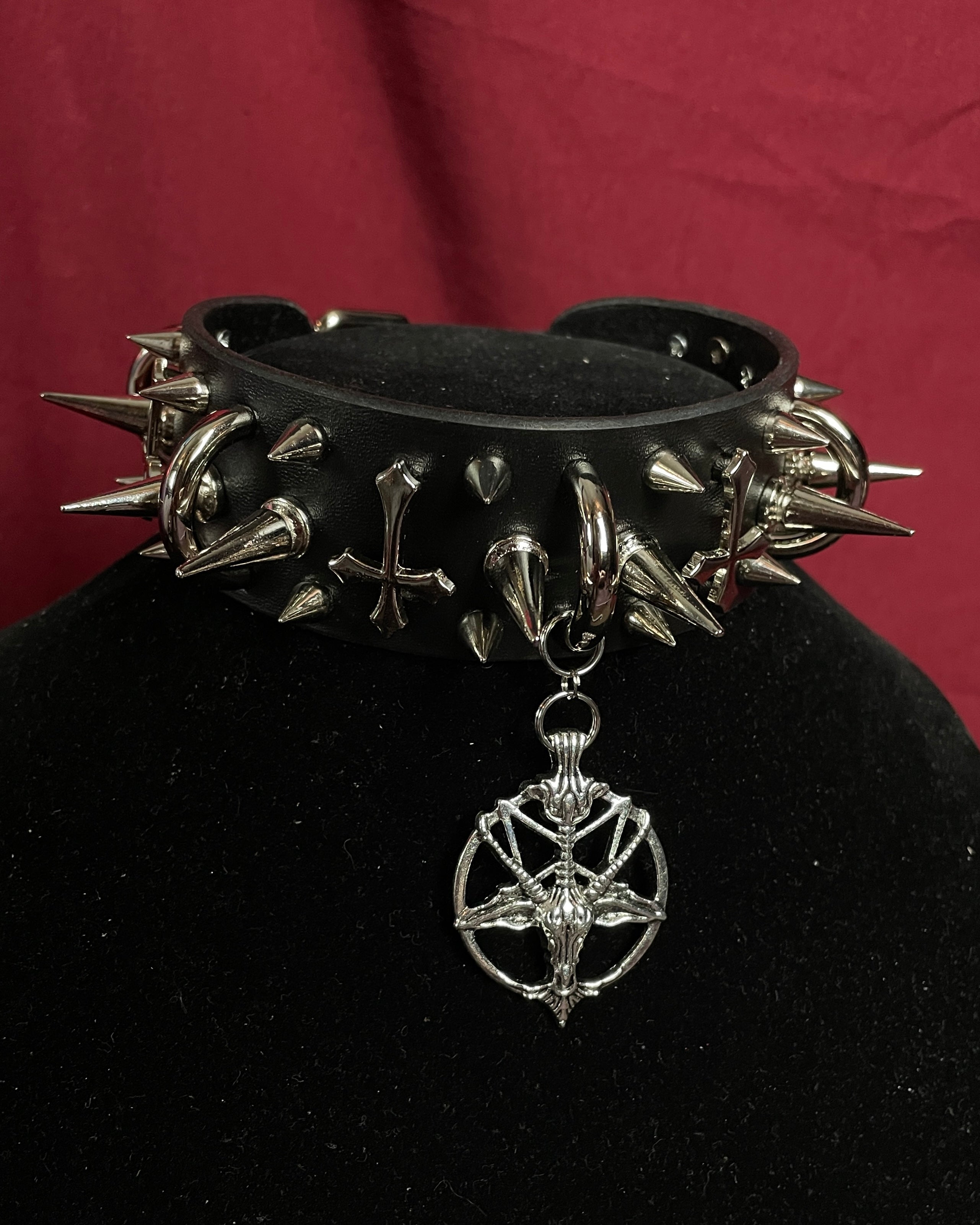 Black spiked collar with a silver pendant on a black stand against a red background