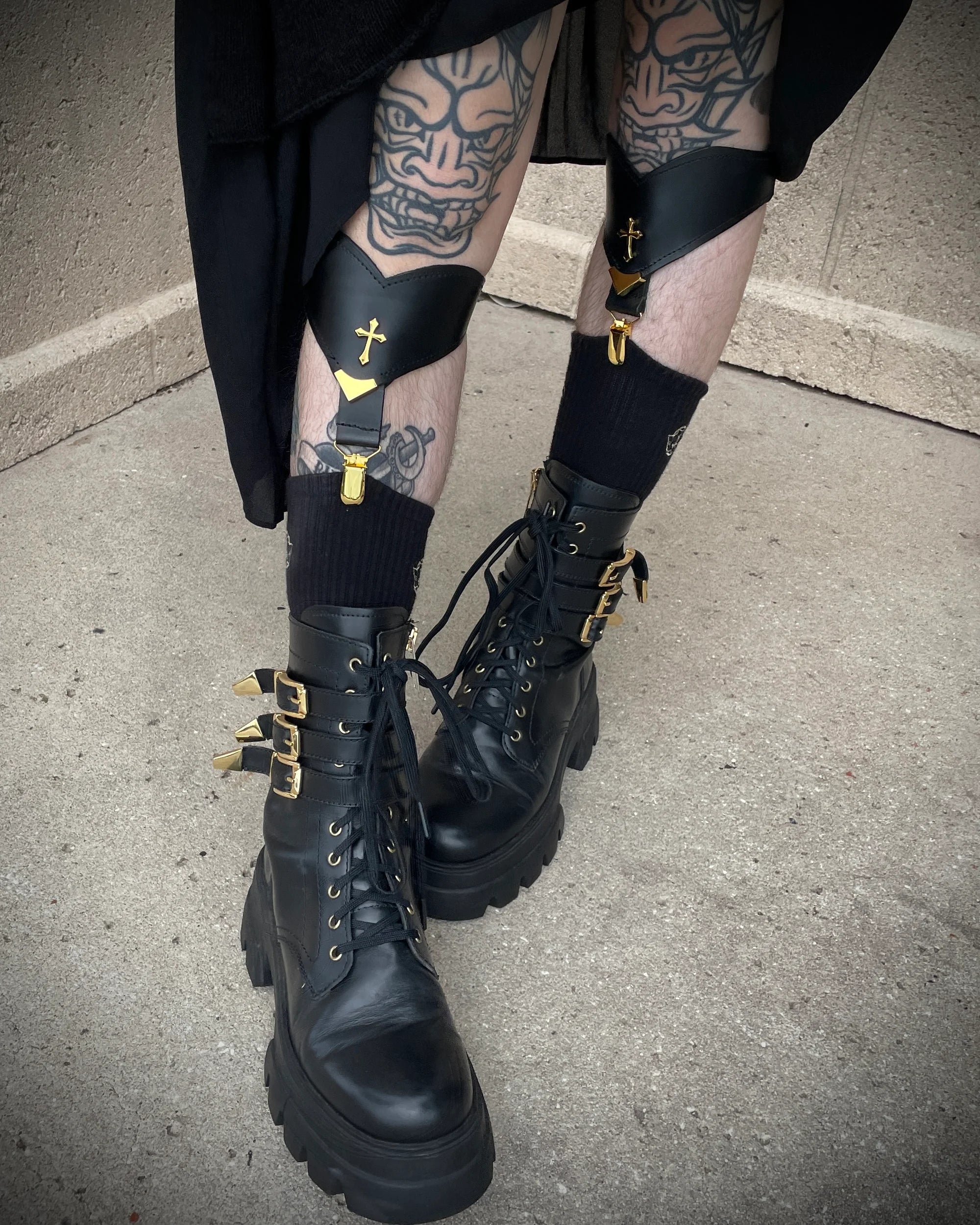 Photo of legs with tattoos wearing large black boots, black socks held up by leather black sock garters.