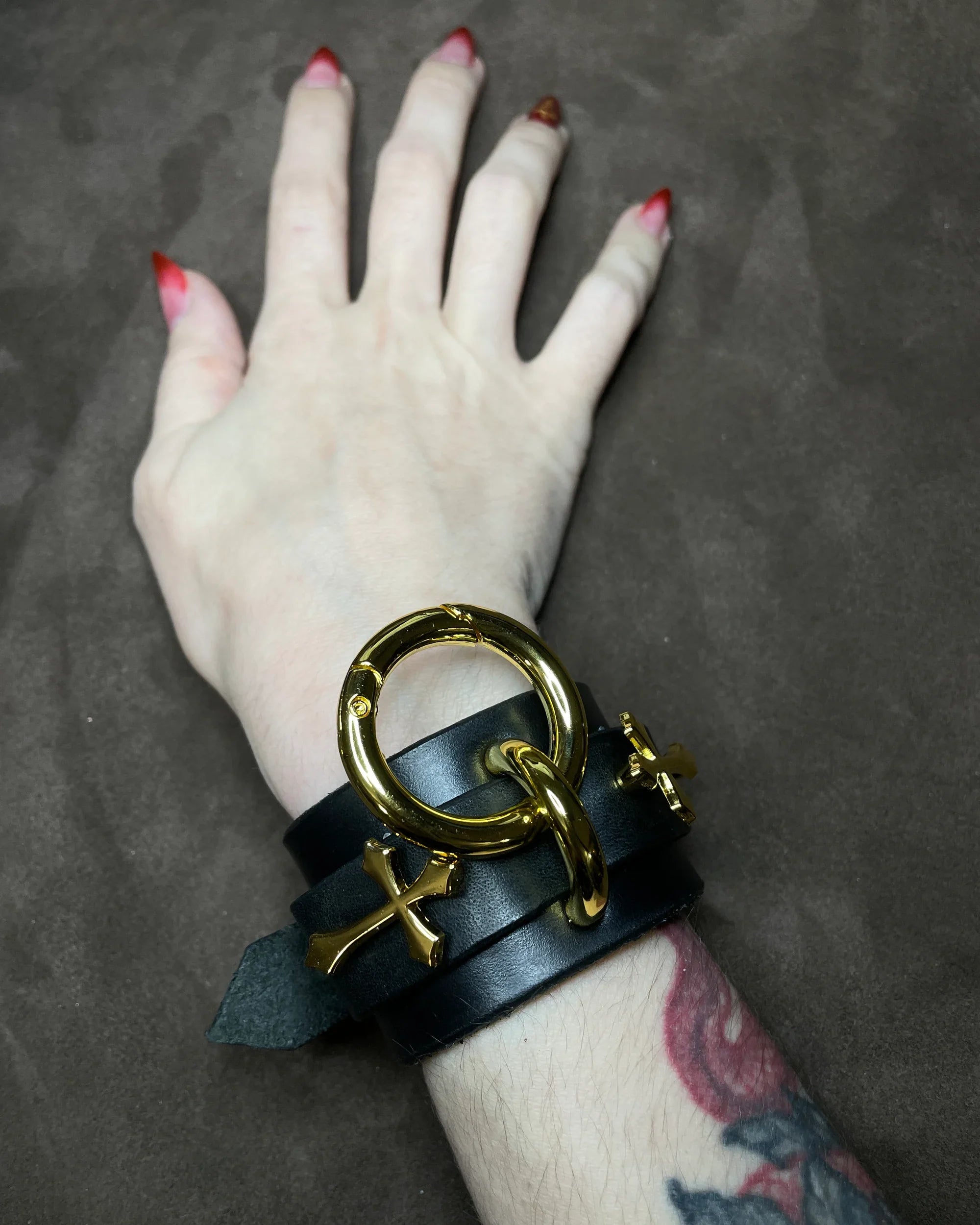 Hand wearing a black leather bracelet with gold accents on a dark background