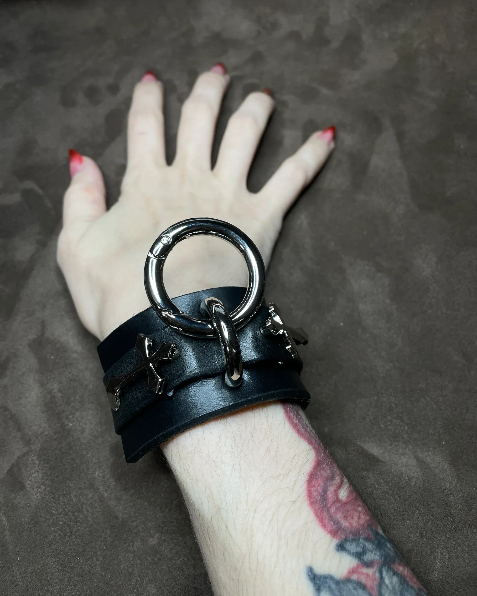 Black leather bracelet with metal ring on a wrist against a dark background