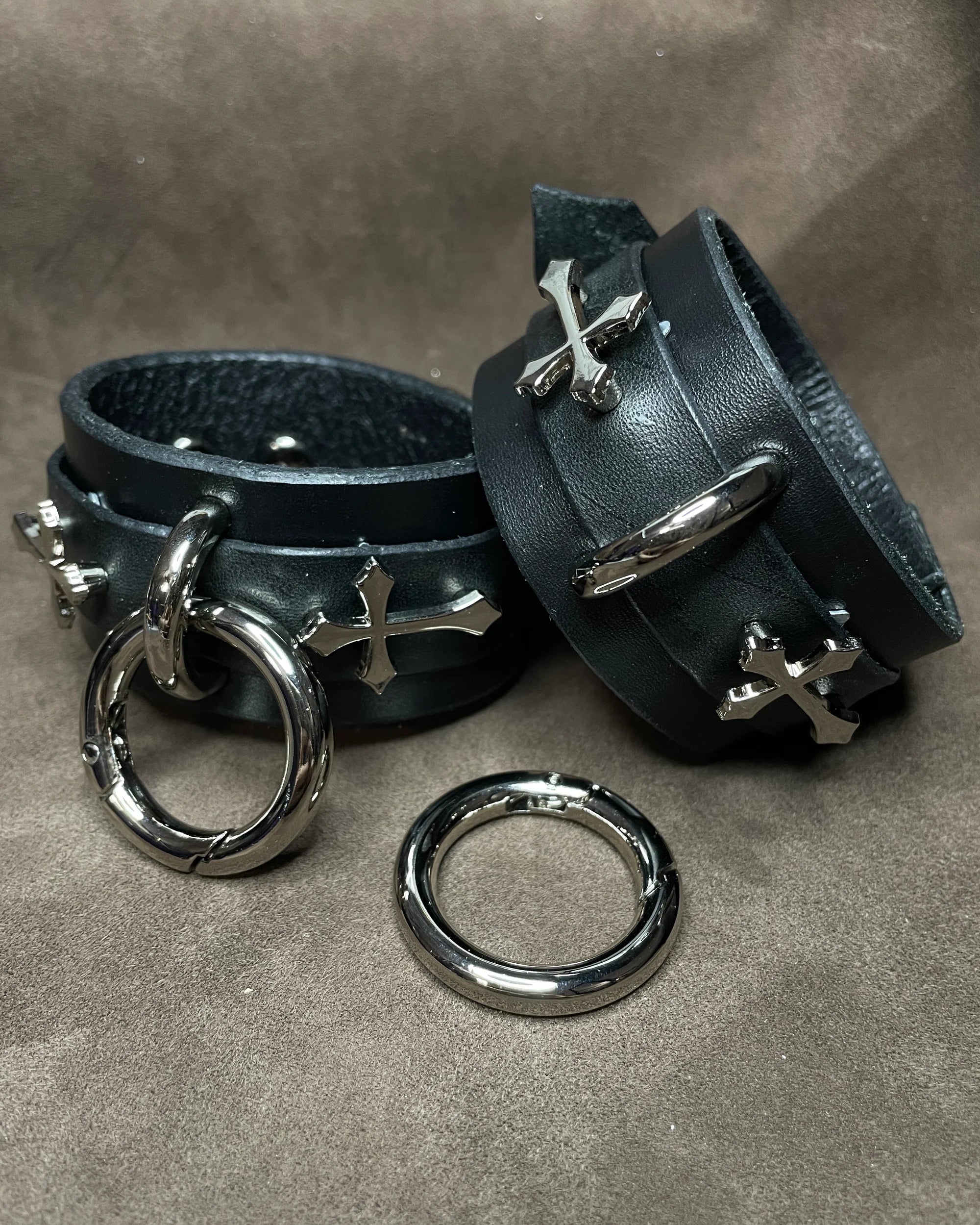 Black leather cuffs with silver rings and crosses on a gray background