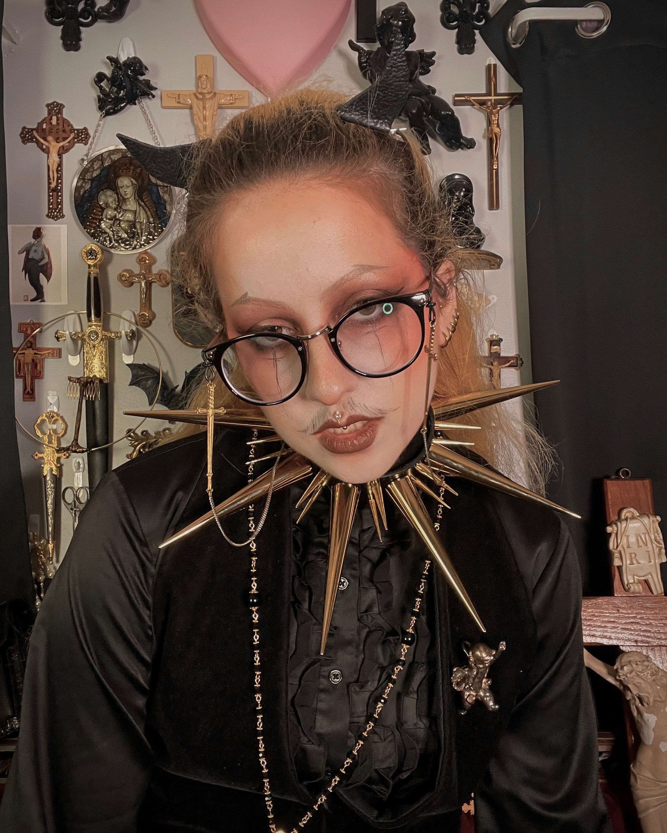 person with blond hair and glasses wearing all black and oversized gold spiked collar