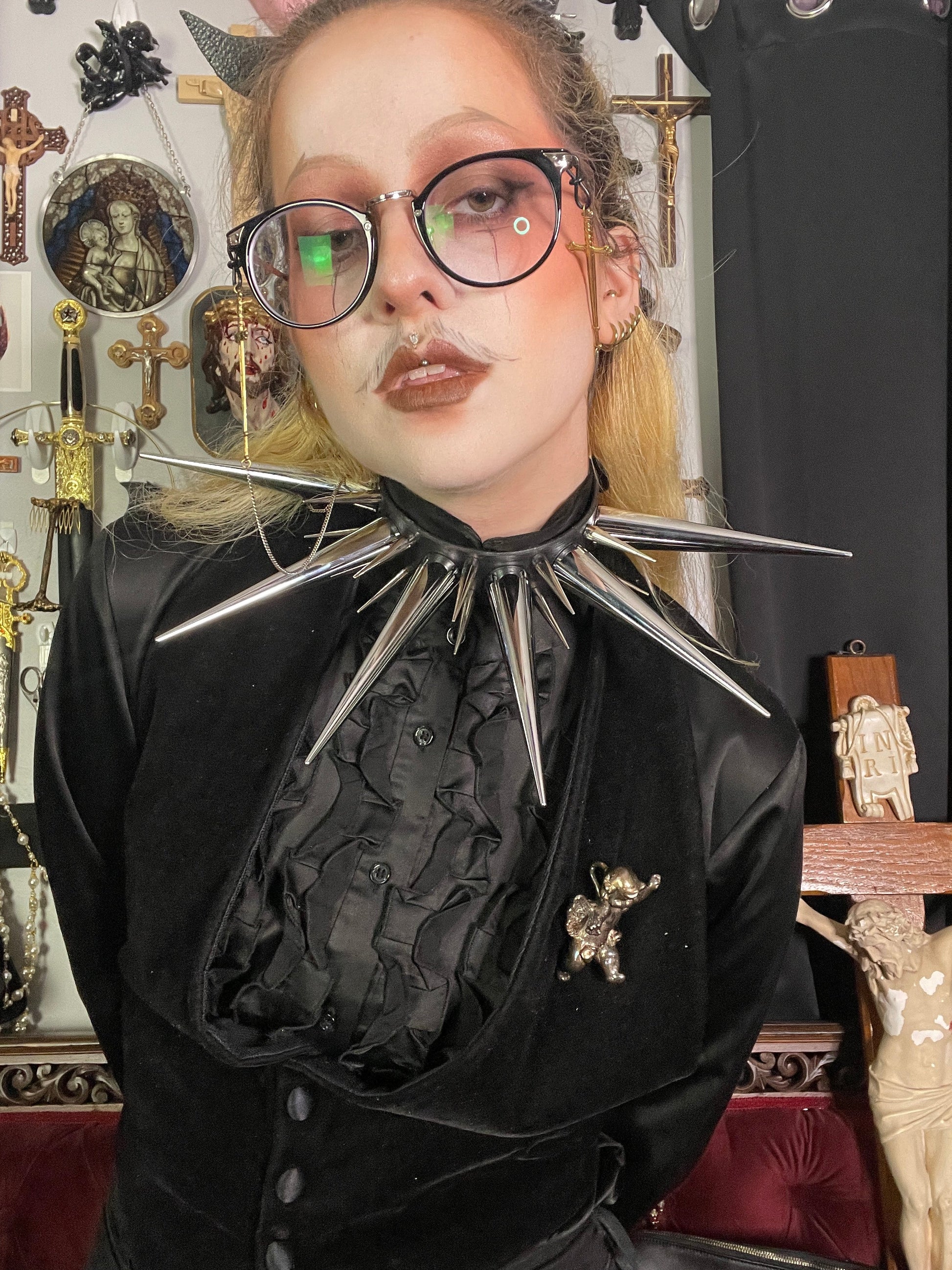 Person with blond hair and glasses wearing all black and oversized spiked collar