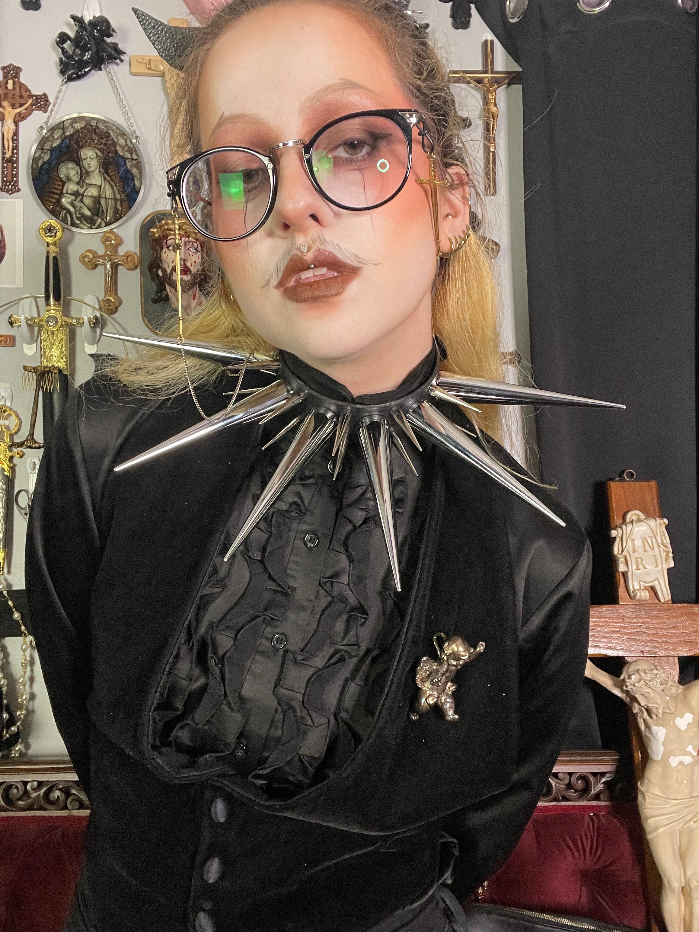 Person with blond hair and glasses wearing all black and oversized spiked collar