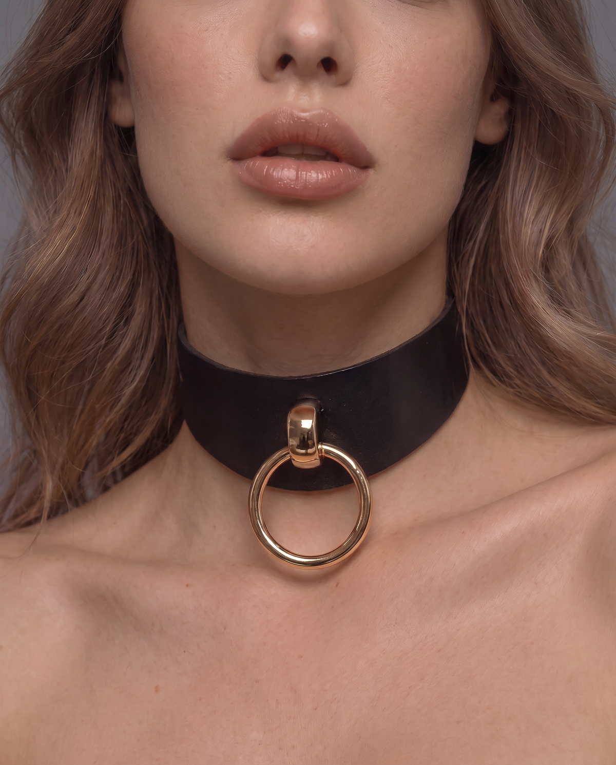 woman wearing a black leather bdsm collar with a large gold  O-ring 