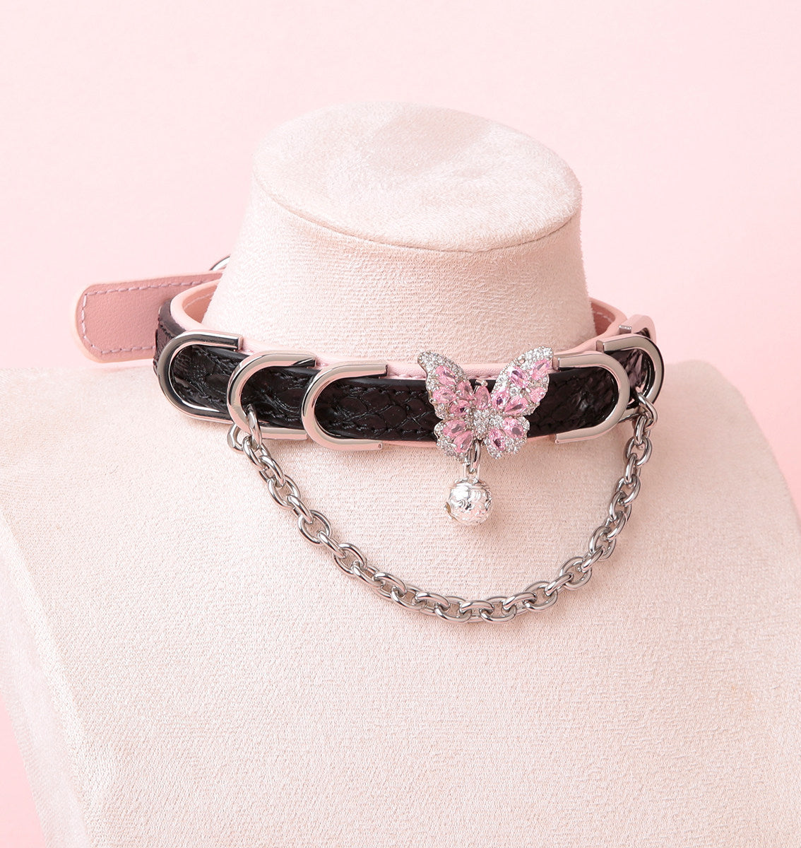black and pink leather collar featuring a silver and pink diamante butterfly charm, silver chain, D rings and bell, displayed on a white mannequin against a pink background.