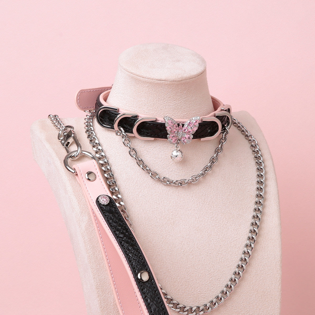 black and pink leather collar and leash set featuring a silver and pink diamante butterfly charm, silver chain, D rings, detachable chain leash and leather hand strap, displayed on a white mannequin against a pink background.