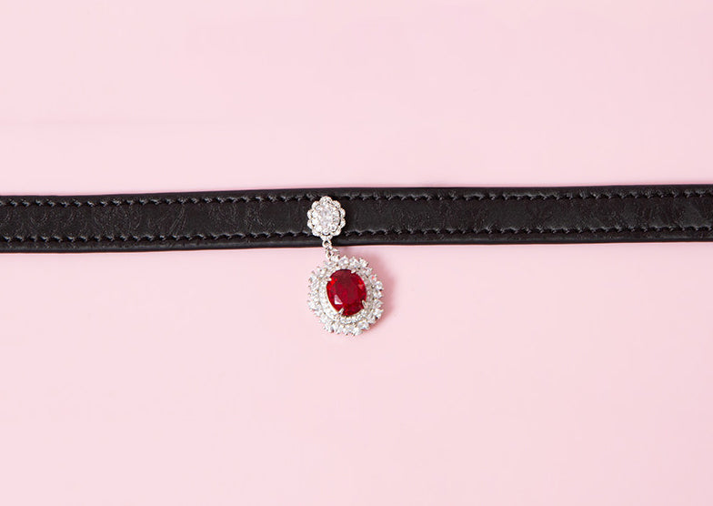 close-up of a black leather collar showing the silver and red crystal cameo pendant, displayed on a pink background.