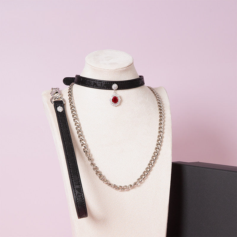 black leather collar and leash set featuring a silver and red crystal cameo pendant, detachable chain leash and leather hand strap, displayed on a white mannequin against a pink background.