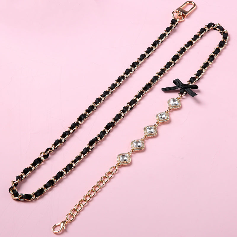 Detachable black and gold crystal and chain leash featuring gold and clear crystal charms, black ribbon bow applique, gold tone chain threaded with black satin ribbon and swivel lobster clasps. Displayed on a pink background.
