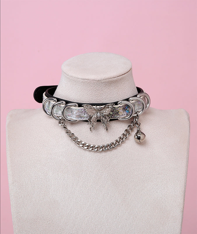 black and holographic silver collar featuring an ornate silver butterfly pendant, silver bell, D rings and chain, displayed on a white mannequin bust against a pink background.