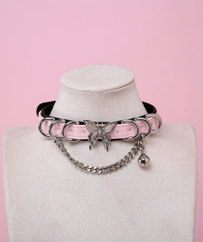 black and pink leather collar featuring an ornate silver butterfly pendant, silver bell, D rings and chain, displayed on a white mannequin bust against a pink background.