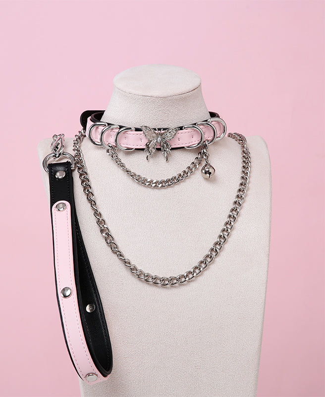 black and pink collar and leash set featuring an ornate silver butterfly pendant, silver bell, D rings and detachable chain leash and leather hand strap, displayed on a white mannequin bust against a pink background.