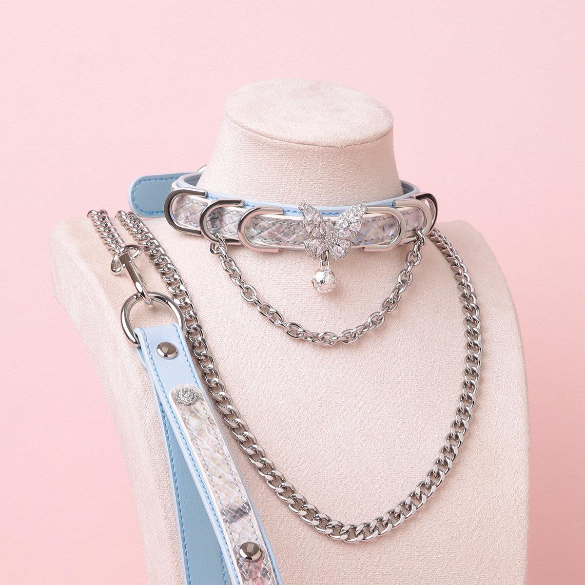 blue and silver leather collar and leash set featuring a silver diamante butterfly charm, D rings, detachable chain leash and leather hand strap, displayed on a white mannequin against a pink background.