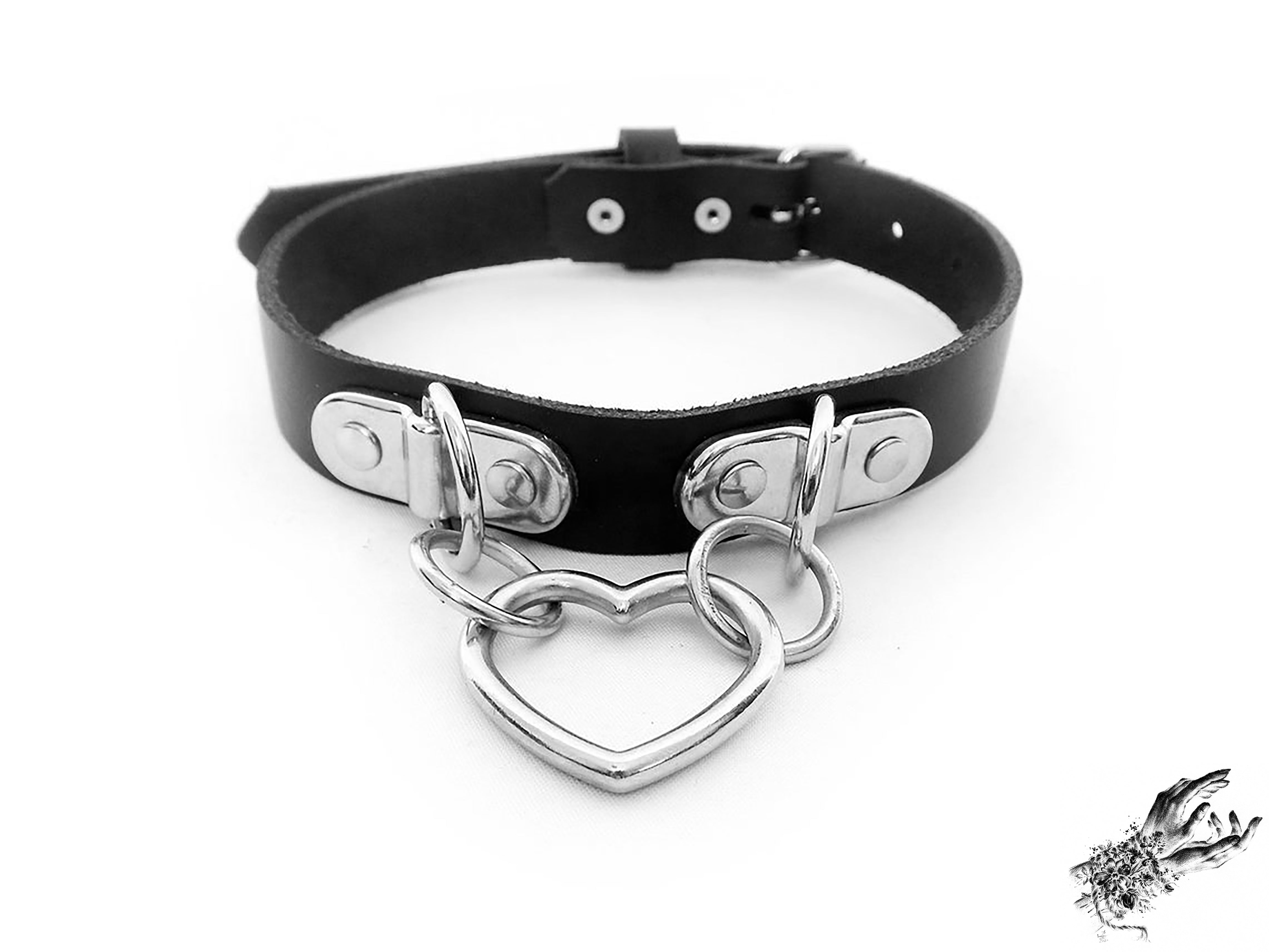 Handmade black leather collar featuring a central silver heart ring suspended by two D ring plates. Displayed on a white background.