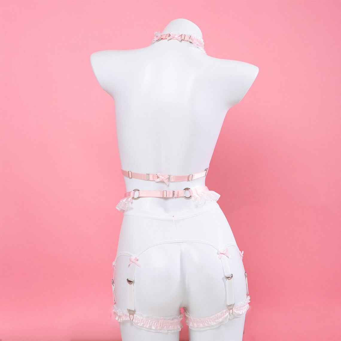 rear view of a pink and white harness set featuring adjustable neck, chest and waist straps, displayed on a white mannequin against a pink background.