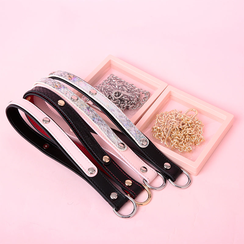 a set of detachable chain leashes and leather hand straps in a variety of colours including black and red, black and pink, pink and holographic silver, and black and holographic silver, displayed on a pink background.