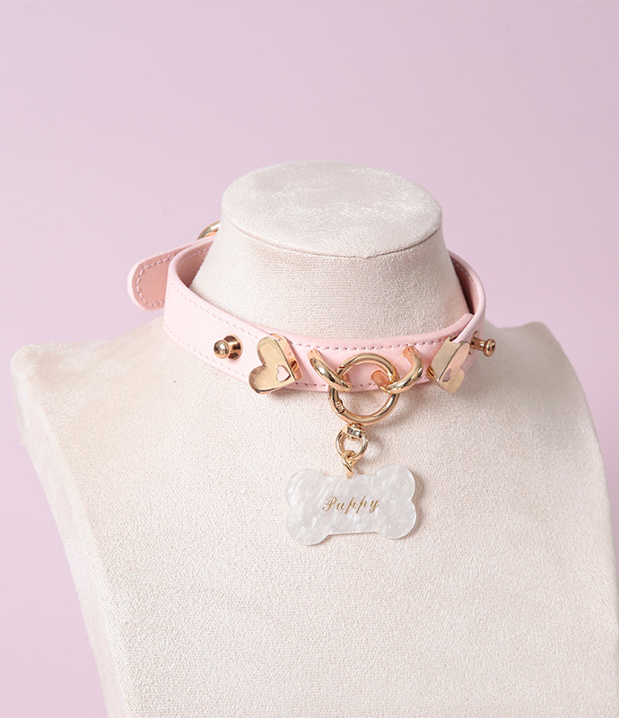 Pink leather collar featuring a central gold tone O ring and custom engraved bone shaped pet tag. Displayed on a mannequin against a pink background.