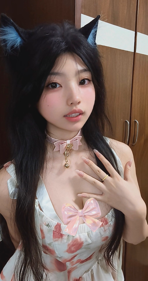customer photo of a pink and gold bow collar featuring gold rose and heart studs with a pink and gold crystal heart and bell pendant, styled with a white and pink floral dress and animal ears for a kawaii aesthetic.