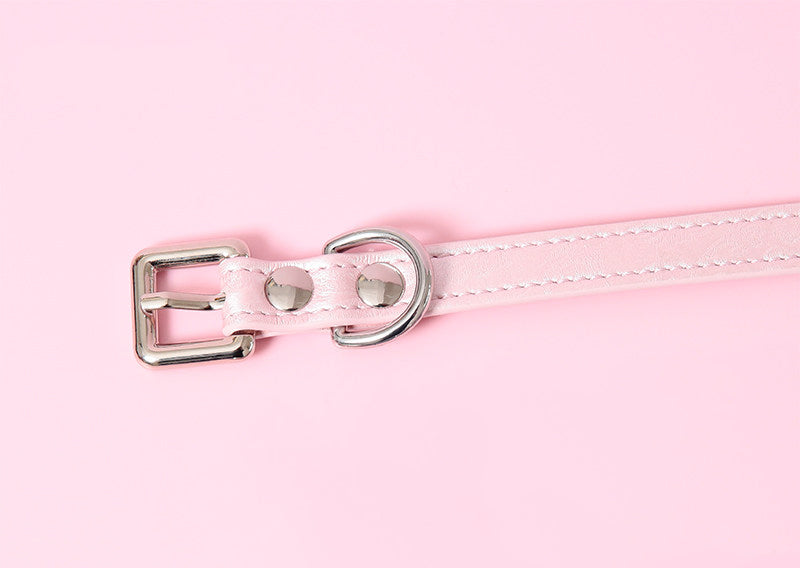 close-up of a pink leather collar showing the stainless steel plated buckle, rivets and D ring, displayed on a pink background.