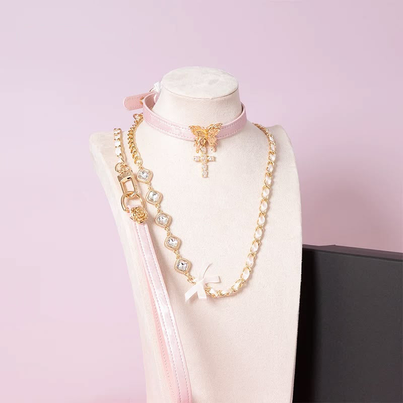 pink and gold collar and leash set featuring a gold tone butterfly pendant, gold and diamante cross charm, detachable diamante and chain leash with pink leather hand strap, displayed on a white mannequin against a pink background.