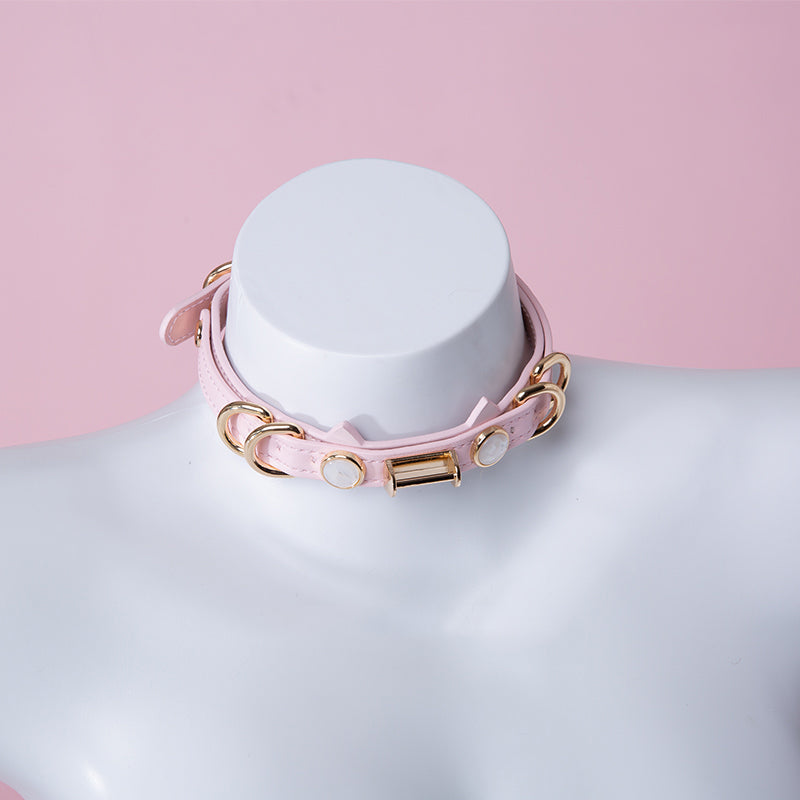 Pink and gold cat girl collar featuring a unique cat ear shaped choker, gold tone hardware and faux mother of pearl studs. Displayed on a mannequin against a pink background.