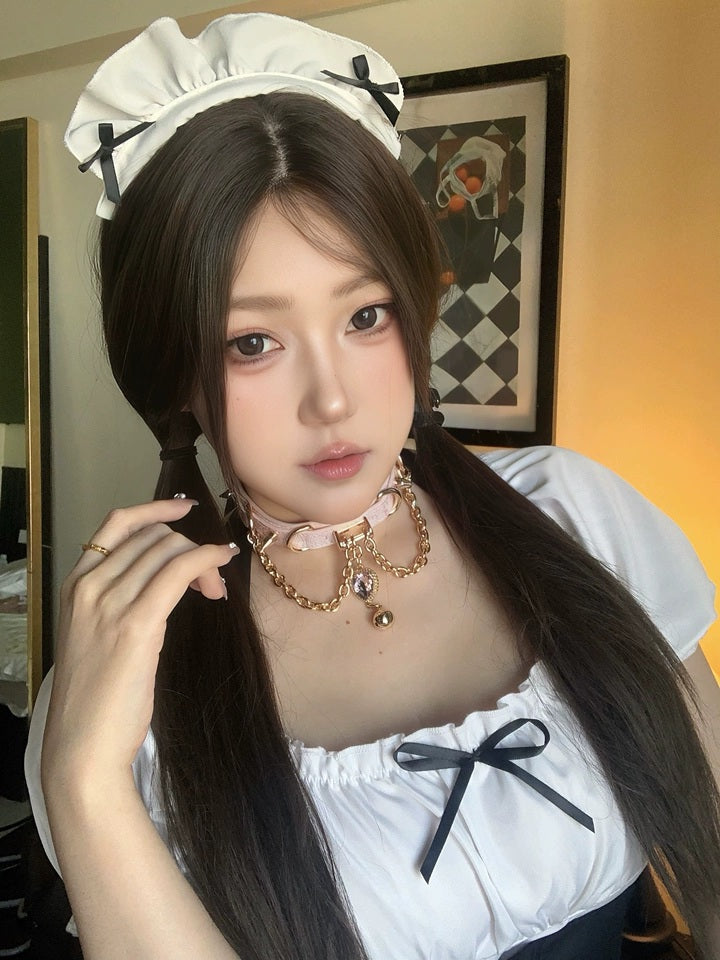 worn photo of a pink and gold leather collar featuring a gold and pink crystal heart charm, gold bell, chains and spike studs, styled with a black and white maid costume for a kawaii aesthetic.