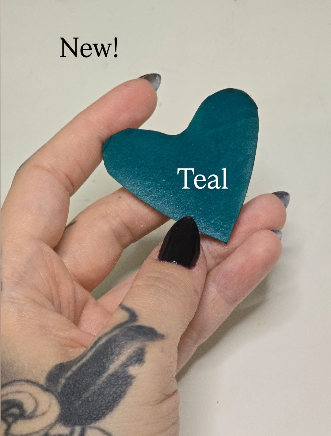 Hand holding teal colored heart with words "new!" And "teal"