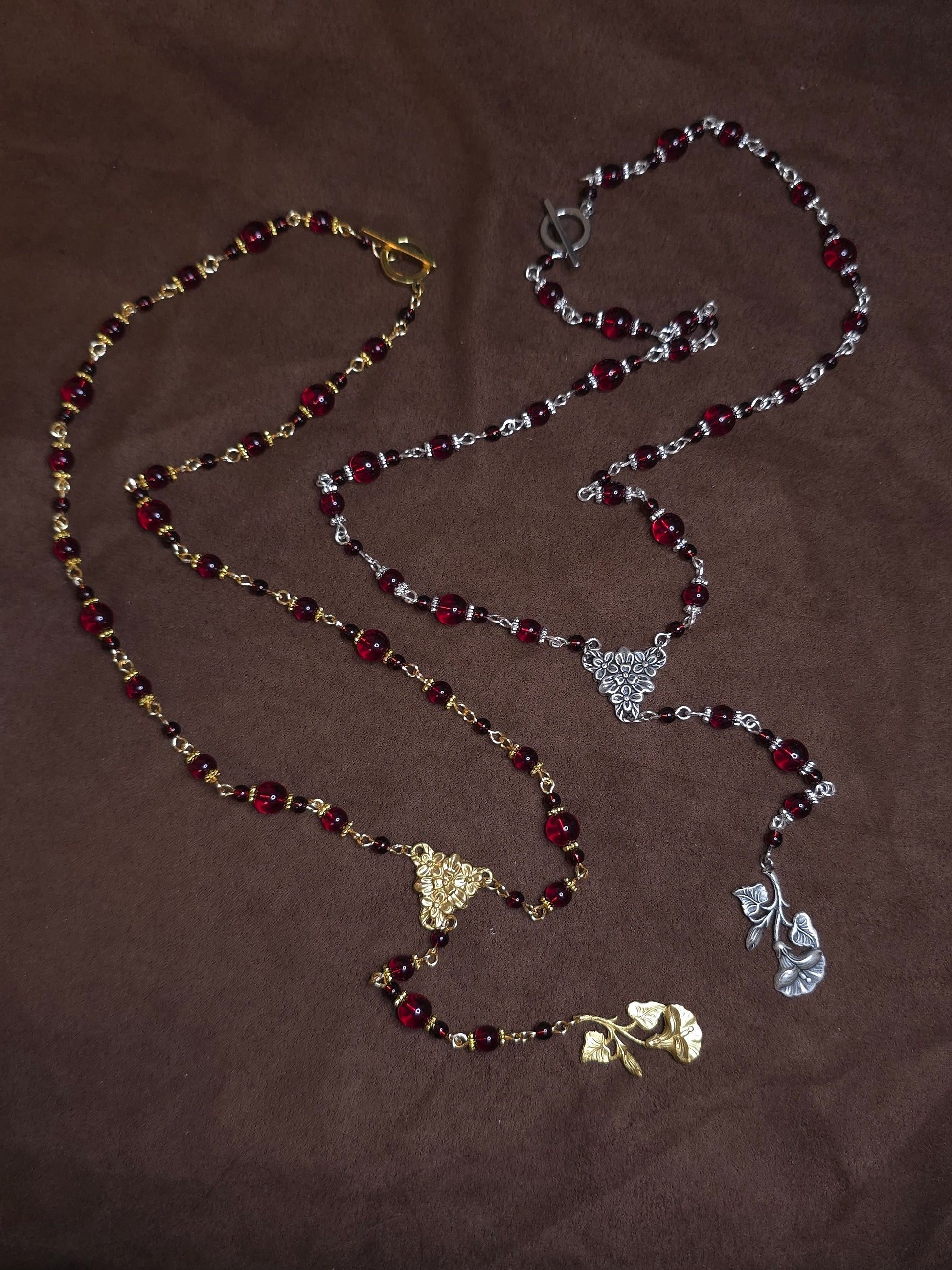 Two necklaces with red beads and gold and silver pendants on a brown background