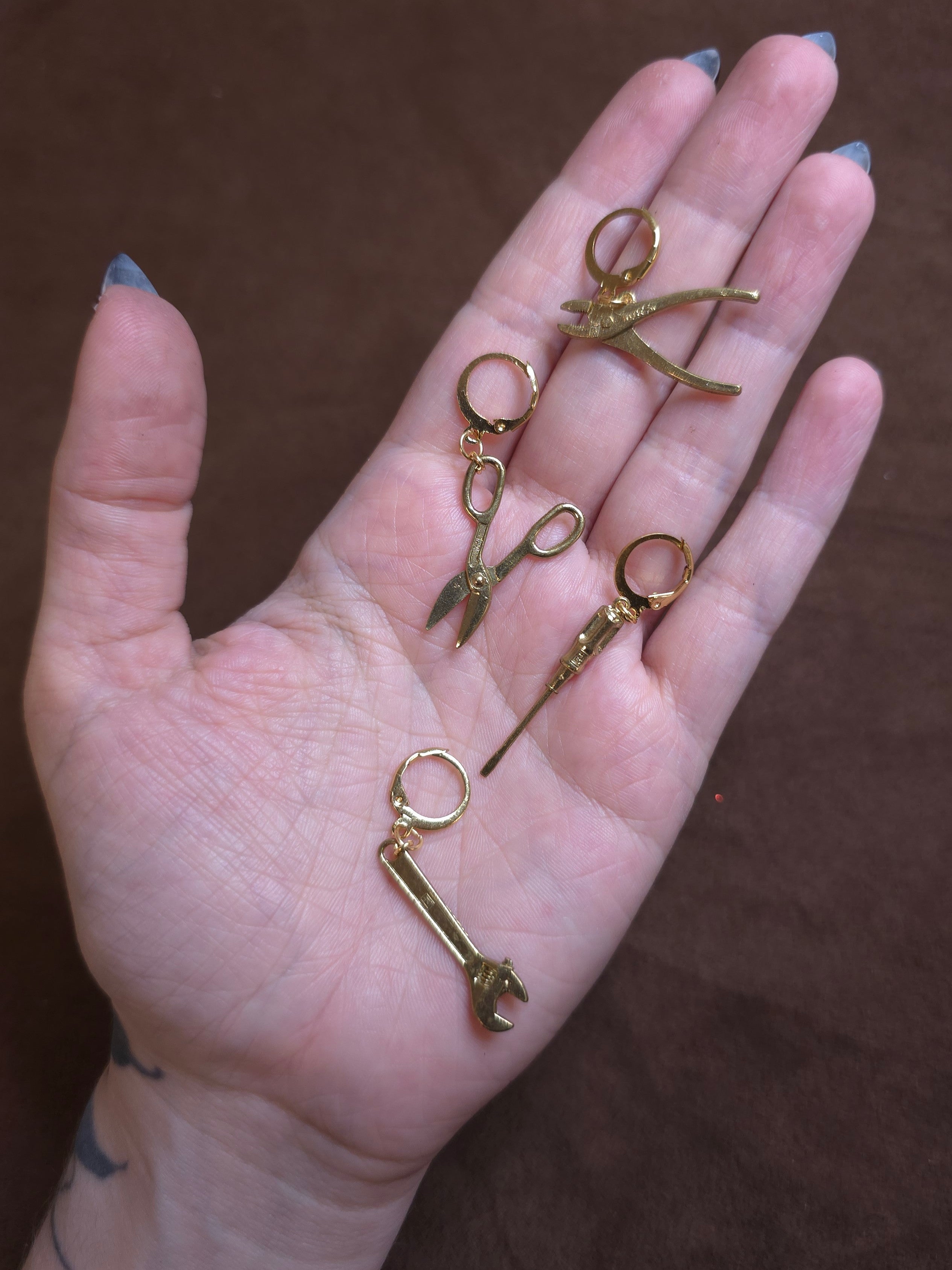 Hand holding small gold jewelry pieces against a brown background