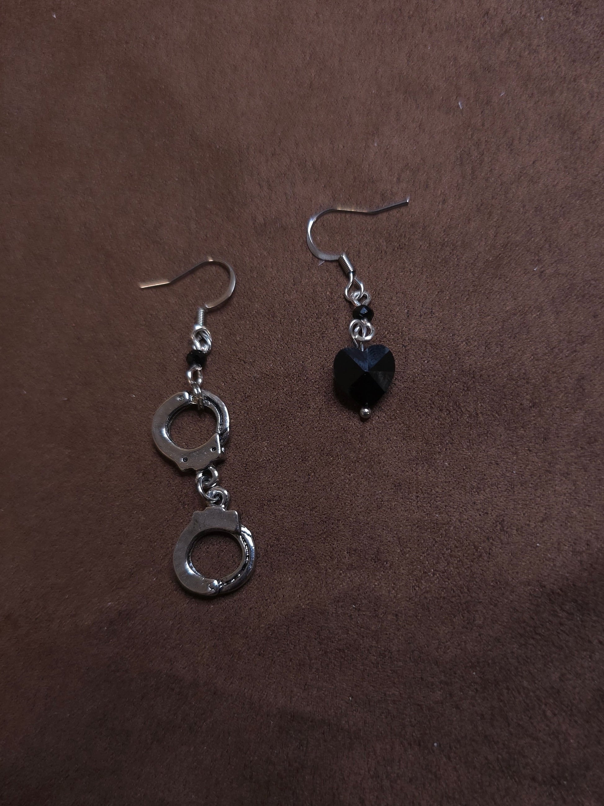 Pair of silver handcuff-shaped earrings with a black heart charm on a brown background