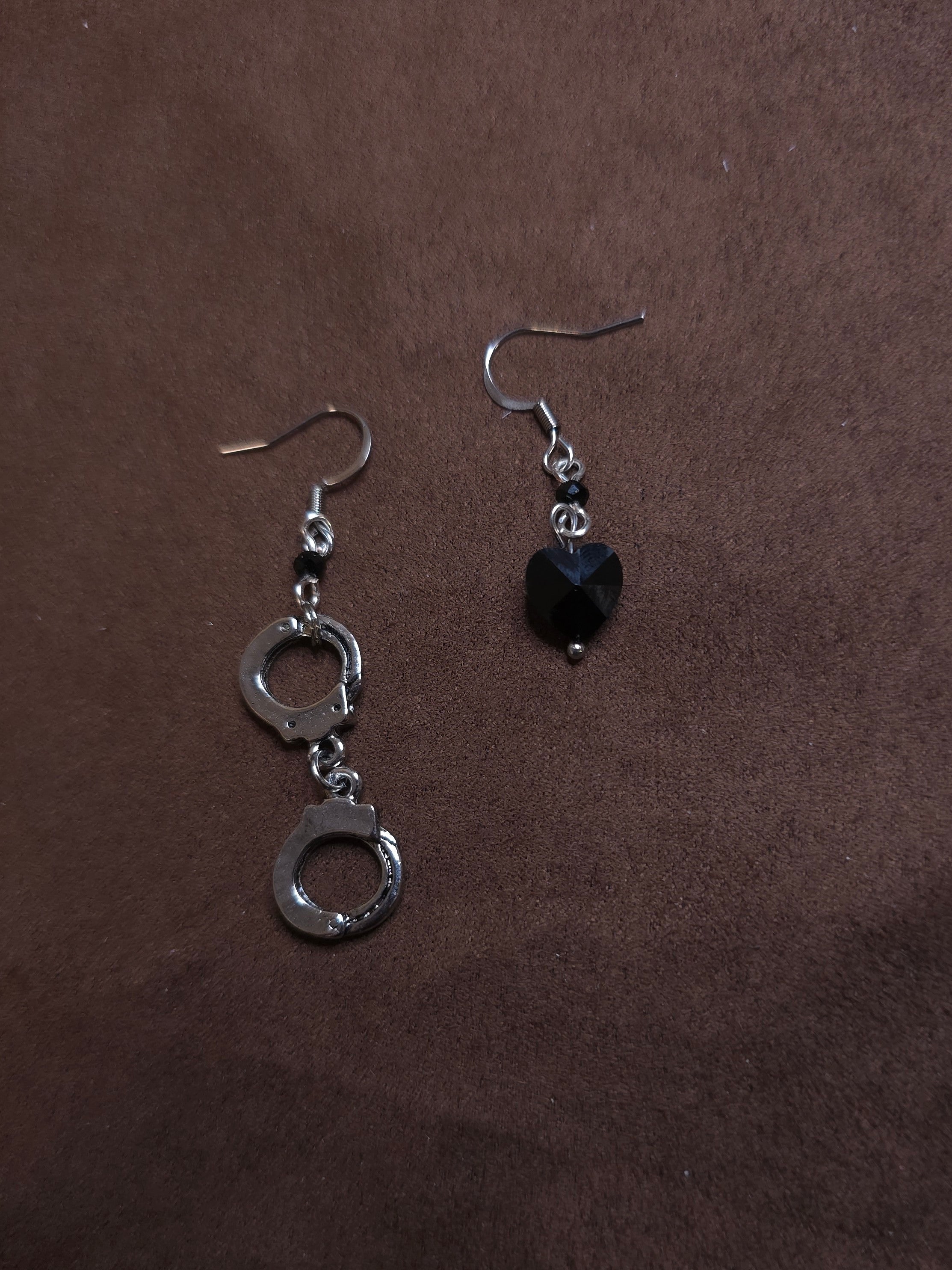 Pair of silver handcuff-shaped earrings with a black heart charm on a brown background