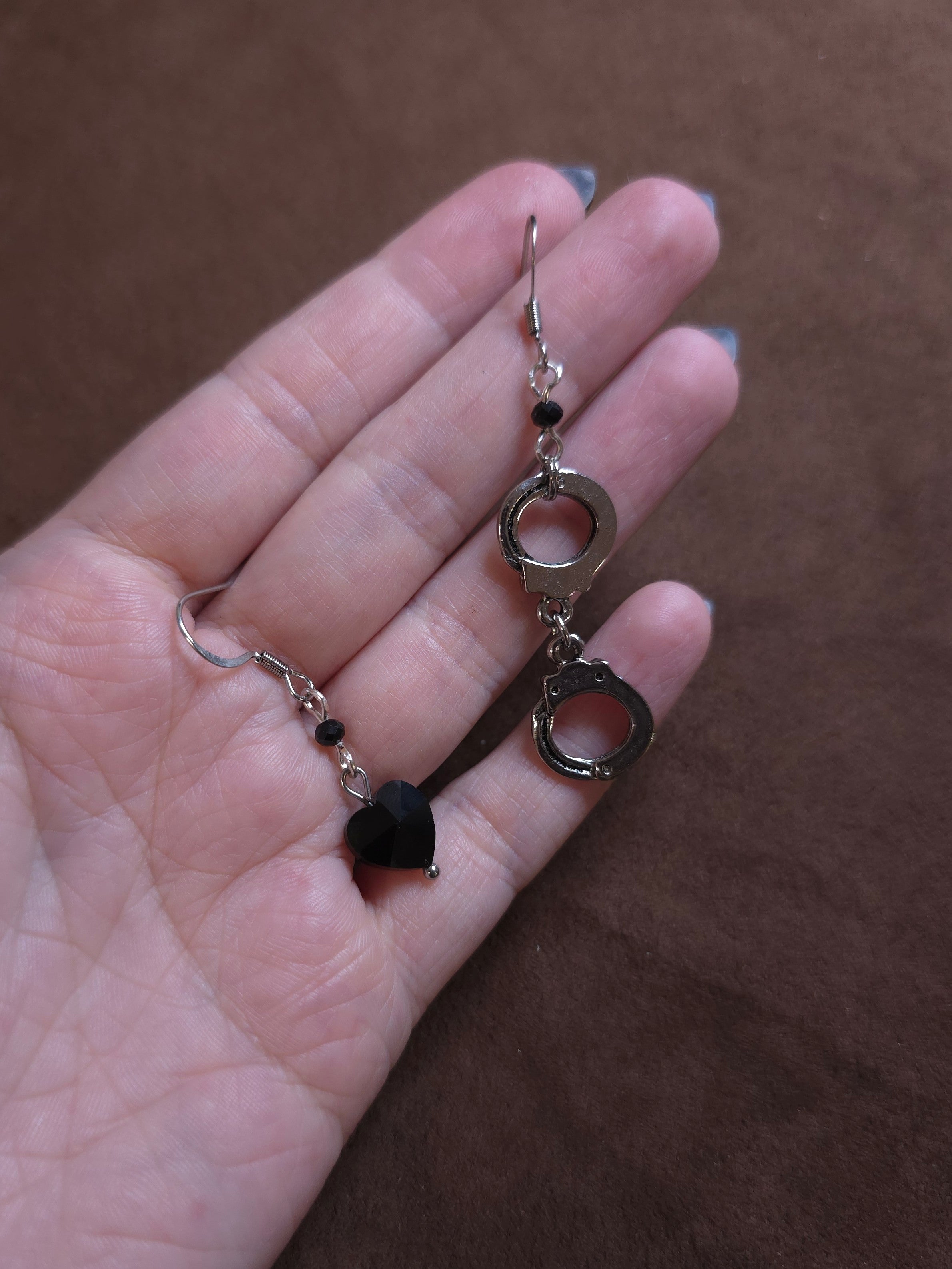 Hand holding hand cuff and black heart earrings