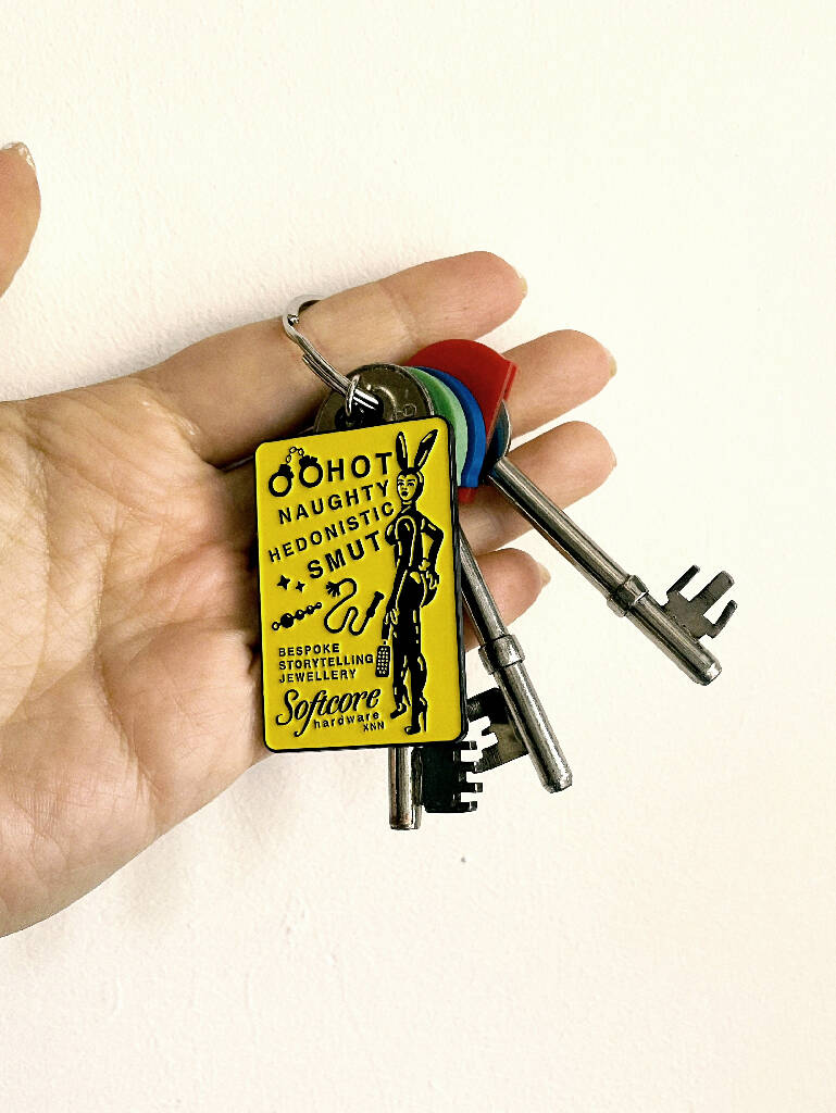 A woman with a necklace chain with a pendant of a yellow keyring with black images and text depicting a rabbit dominatrix with a whip and anal beads.